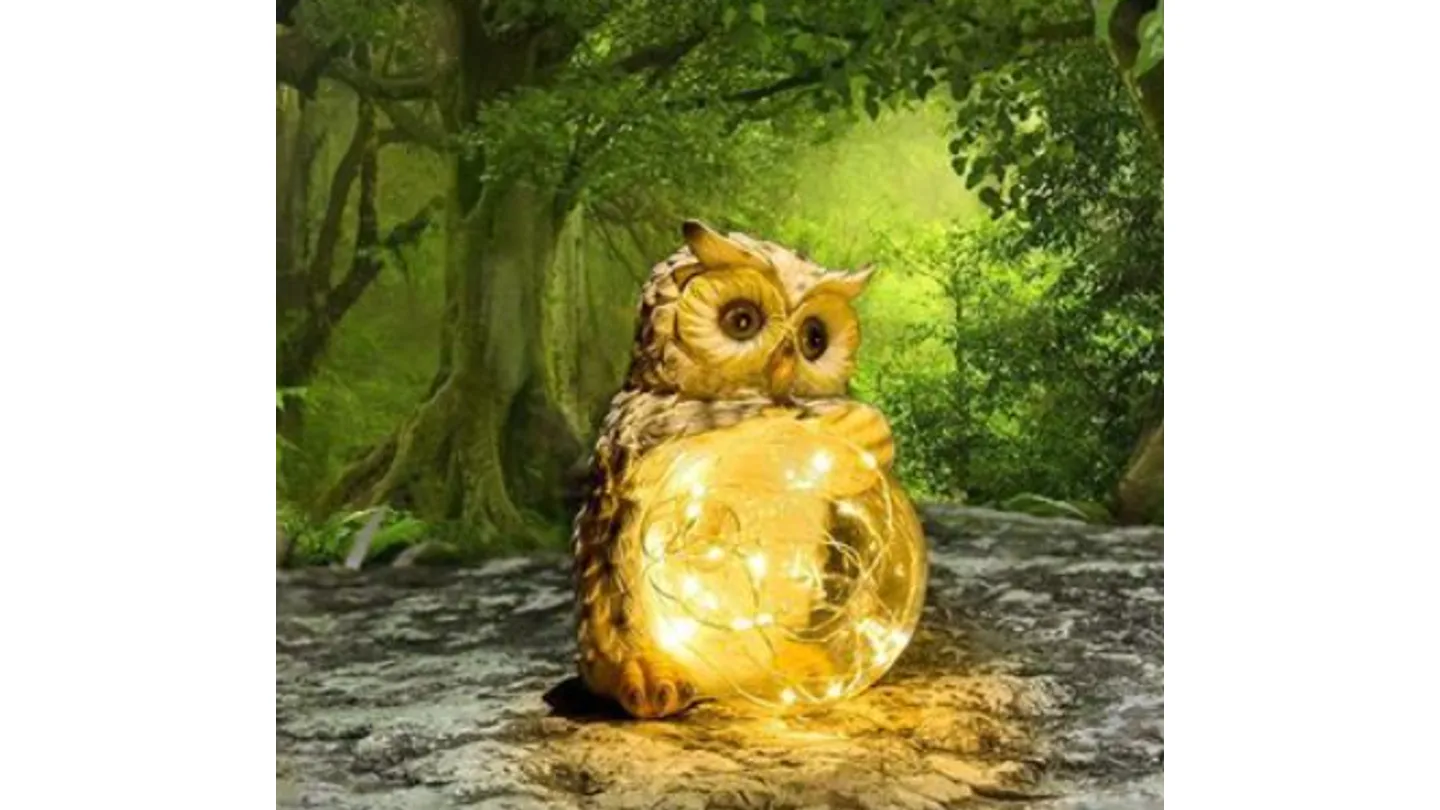 Solar LED owl garden light illuminated in a forest setting.