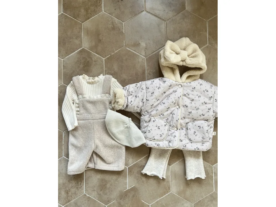 A beige floral quilted hooded jacket with a bow, displayed with a ribbed top, leggings, and a beret.