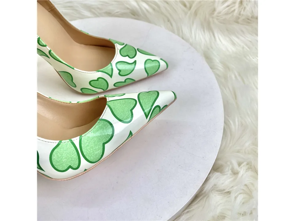 Close-up of the pointed toe of the white and green heart-patterned stiletto pumps.