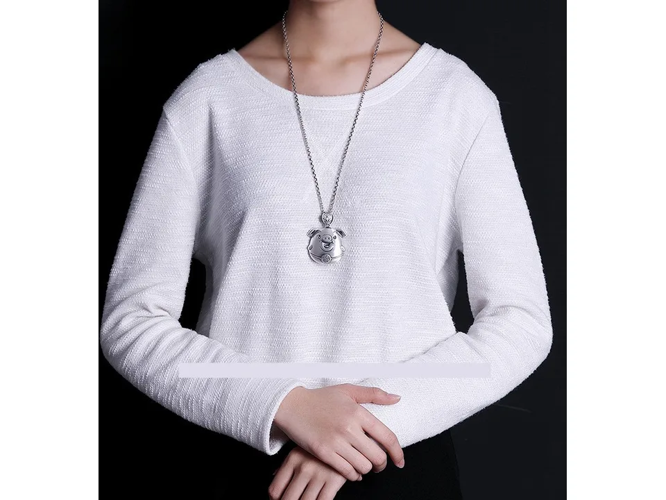 A person wearing a silver chain necklace with a pig pendant.