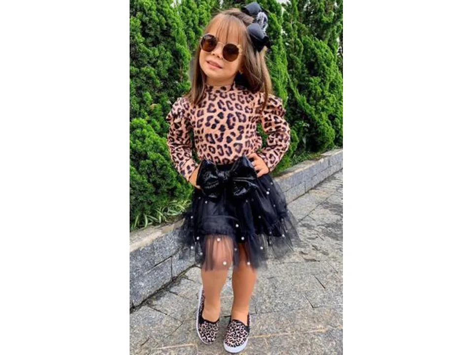 A young girl wearing a leopard print long sleeve top and a black tulle skirt with a large bow.
