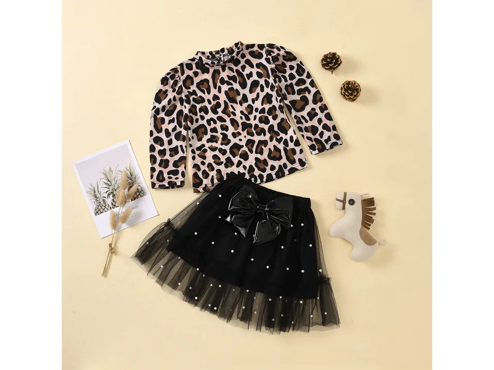 A leopard print long sleeve top and a black tulle skirt with a large bow laid out on a flat surface.