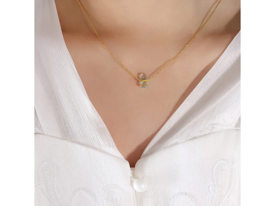 A woman wearing a gold necklace with a light blue rectangular crystal pendant.
