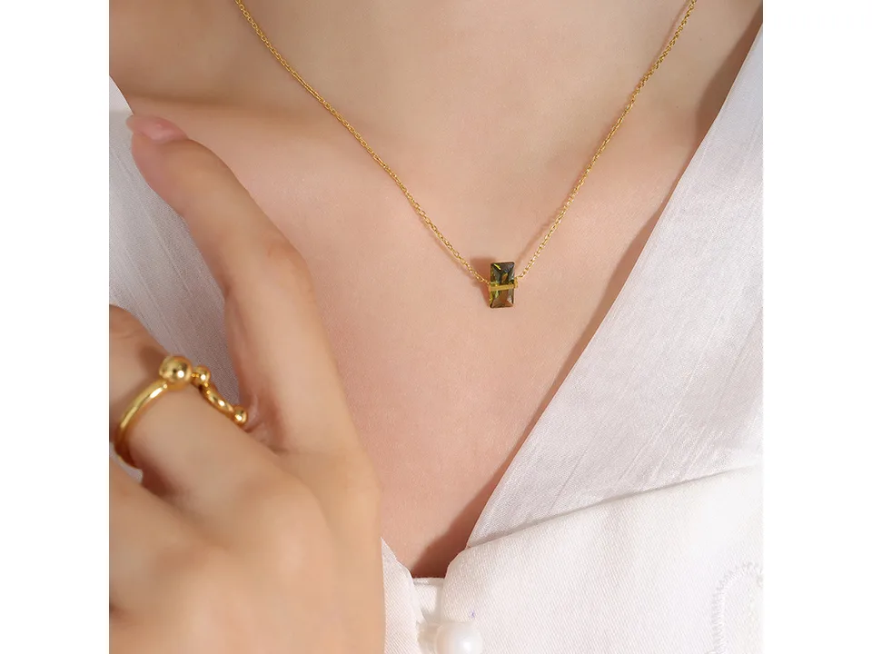 A woman wearing a gold necklace with a green rectangular crystal pendant.