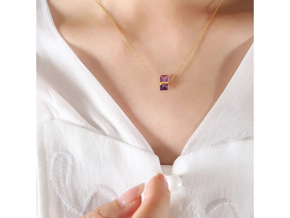 A woman wearing a gold necklace with a purple rectangular crystal pendant.