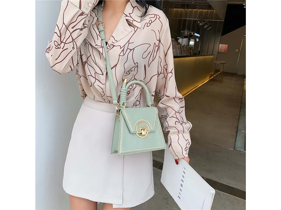 A woman wearing a light green small square crossbody bag with a gold lock closure.