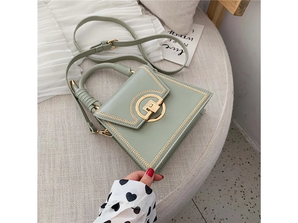 Close-up of a light green small square handbag with gold embroidery and a gold lock closure.