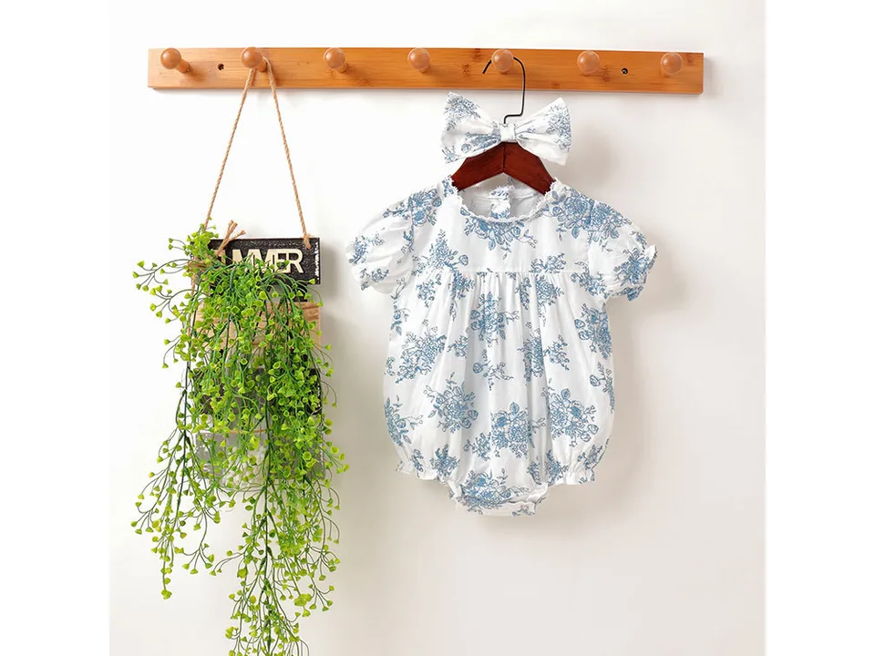Baby girl floral romper and matching headband hanging on a wooden rack.