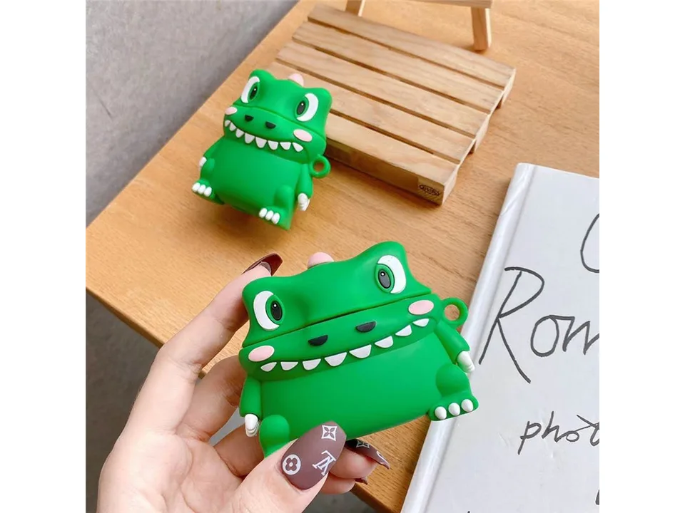 A hand holding a green dinosaur-shaped silicone case for wireless earphones.