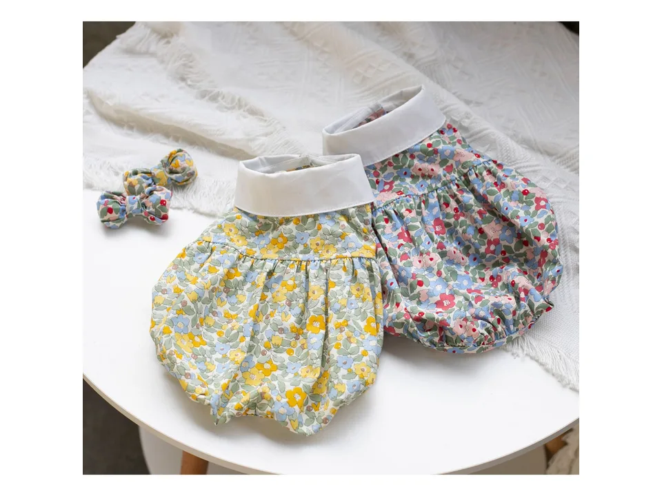 Two floral dog dresses with white collars and matching hair bows on a white table.