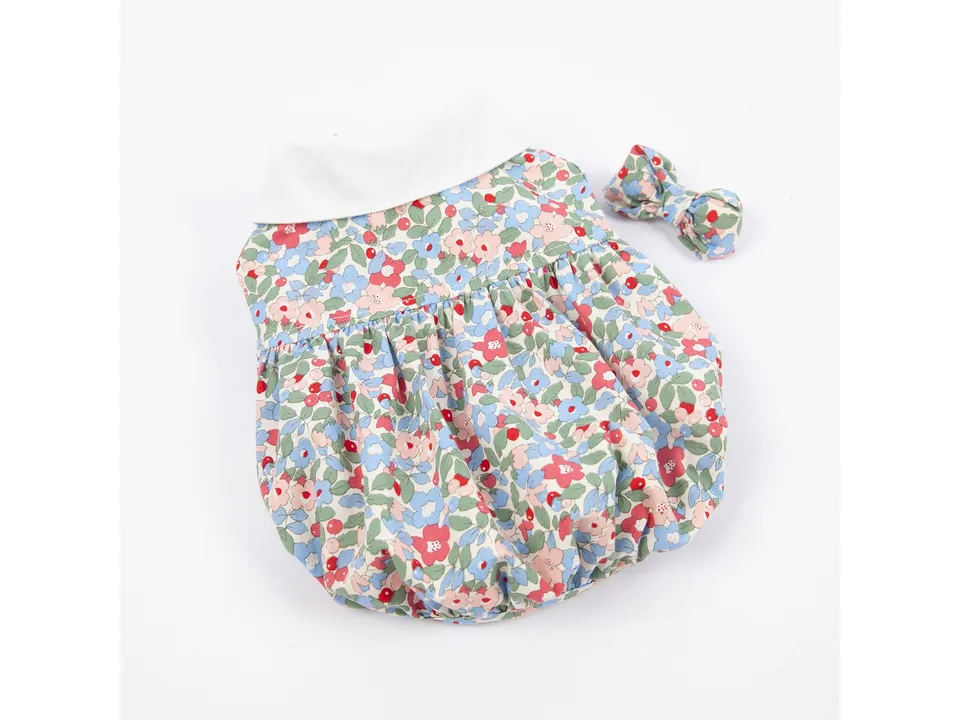 A blue and pink floral dog dress with a white collar and a matching hair bow.