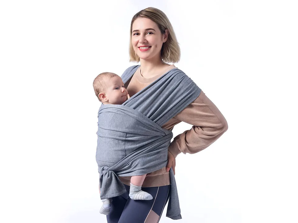 A woman wearing a grey baby sling carrier with a baby inside.