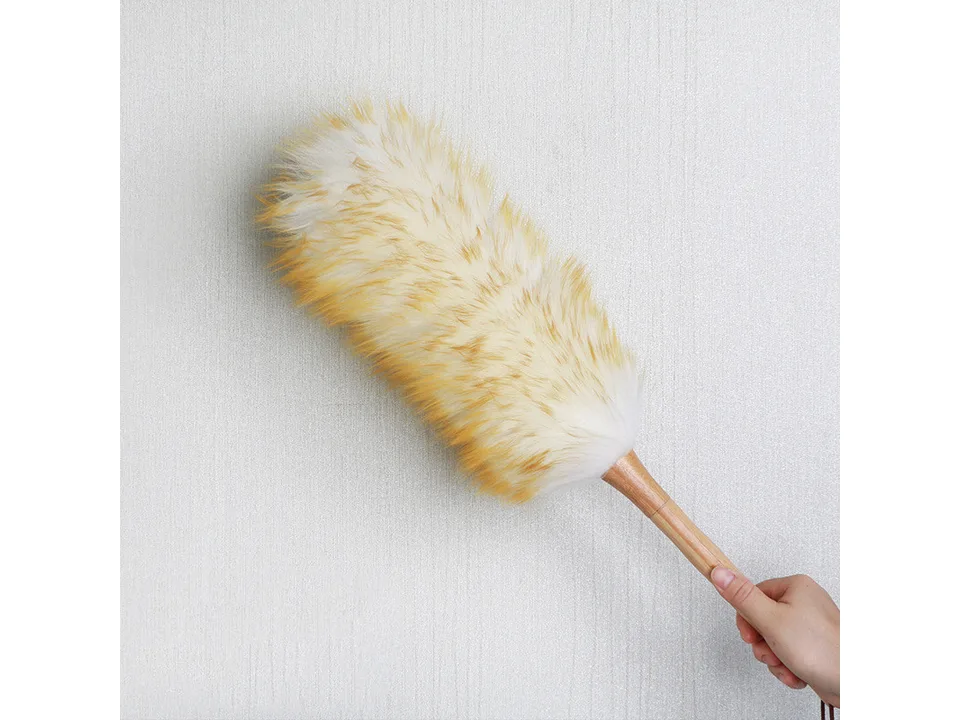 A hand holding a wool duster with a wooden handle.