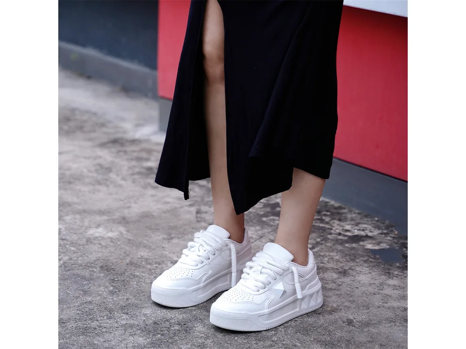 A person wearing white platform sneakers with rivet details.