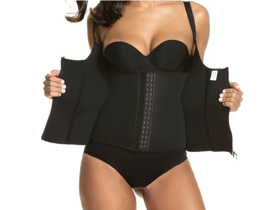 A woman wearing a black waist trainer corset with the outer zipper open to show the inner hook-and-eye closure.