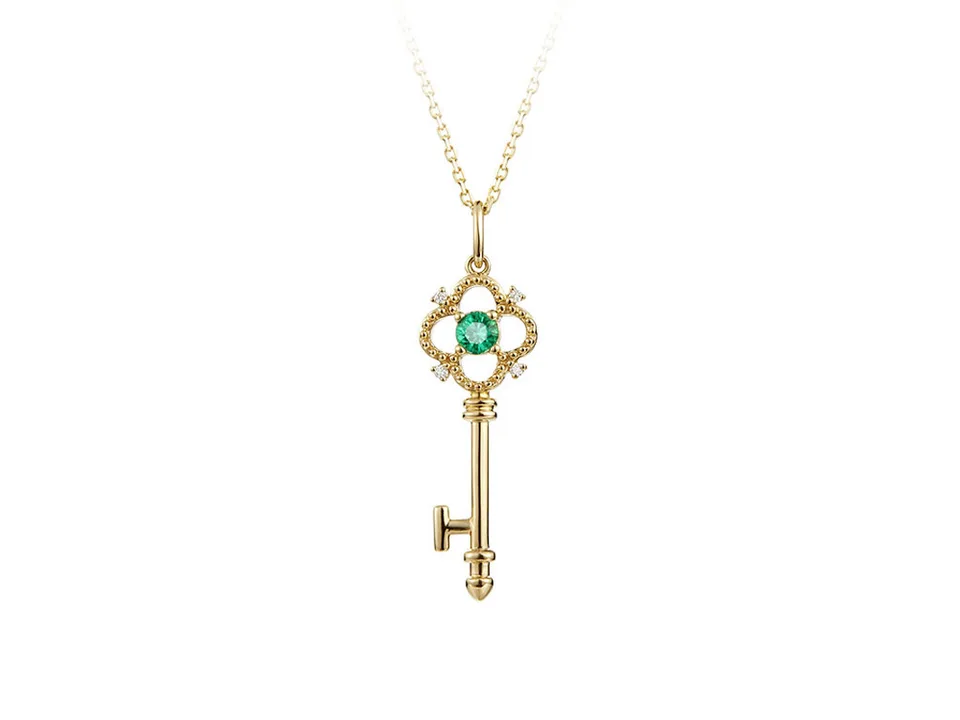 Gold key pendant necklace with a green crystal, isolated on a white background.