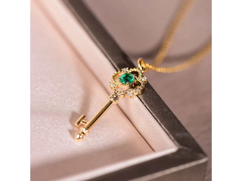 Close-up of a gold key pendant necklace with a green crystal center.