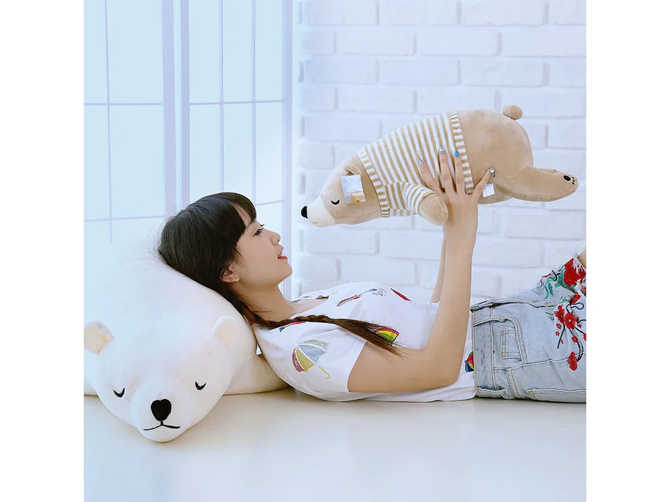 A young woman holding a striped polar bear plush toy above her head while lying next to a larger one.