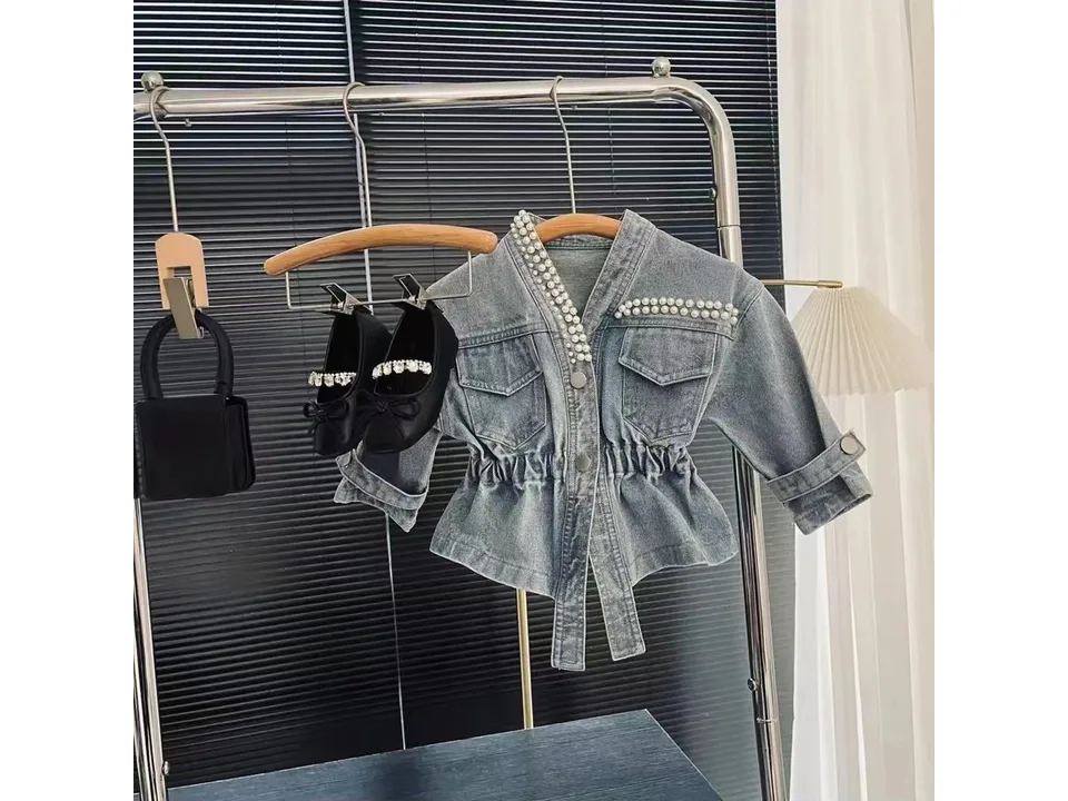 Full view of the denim jacket with pearl details hanging on a rack.