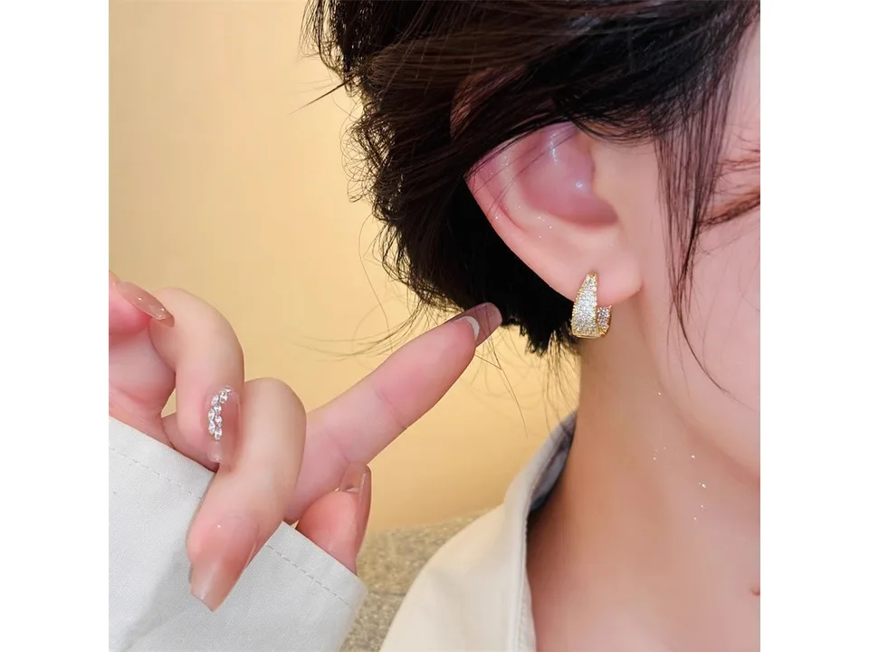A person wearing a gold-tone geometric hoop earring.