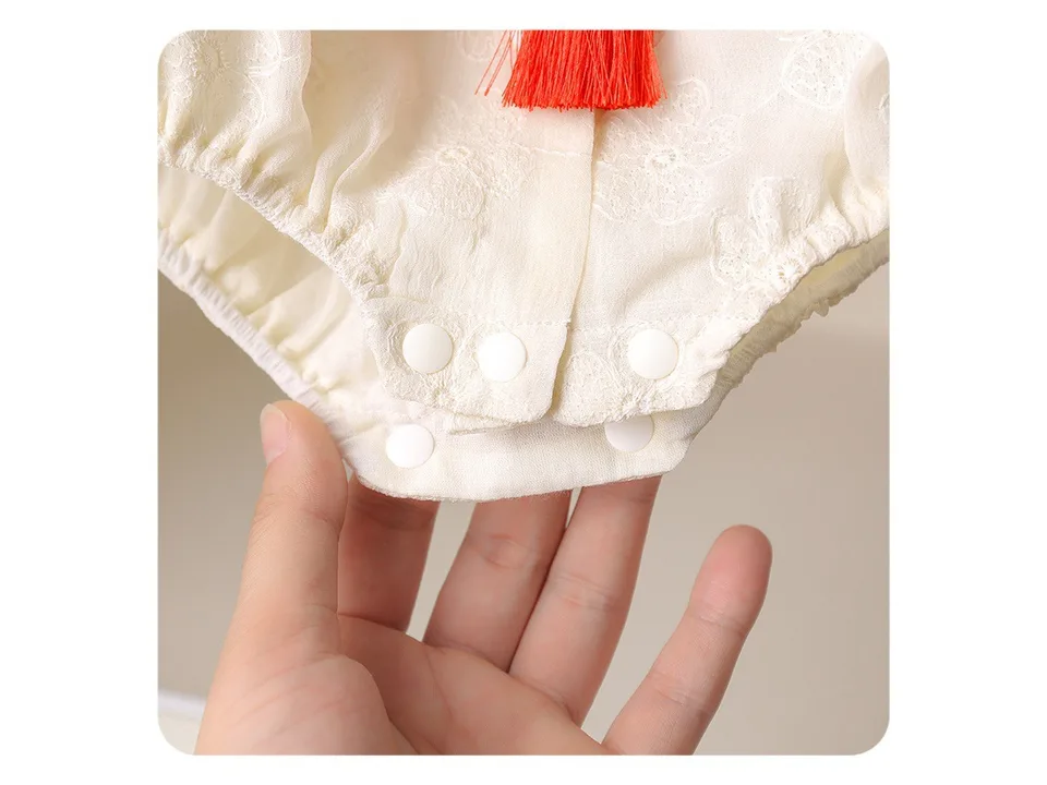 Close-up of the bottom snap buttons on a cream-colored baby romper.