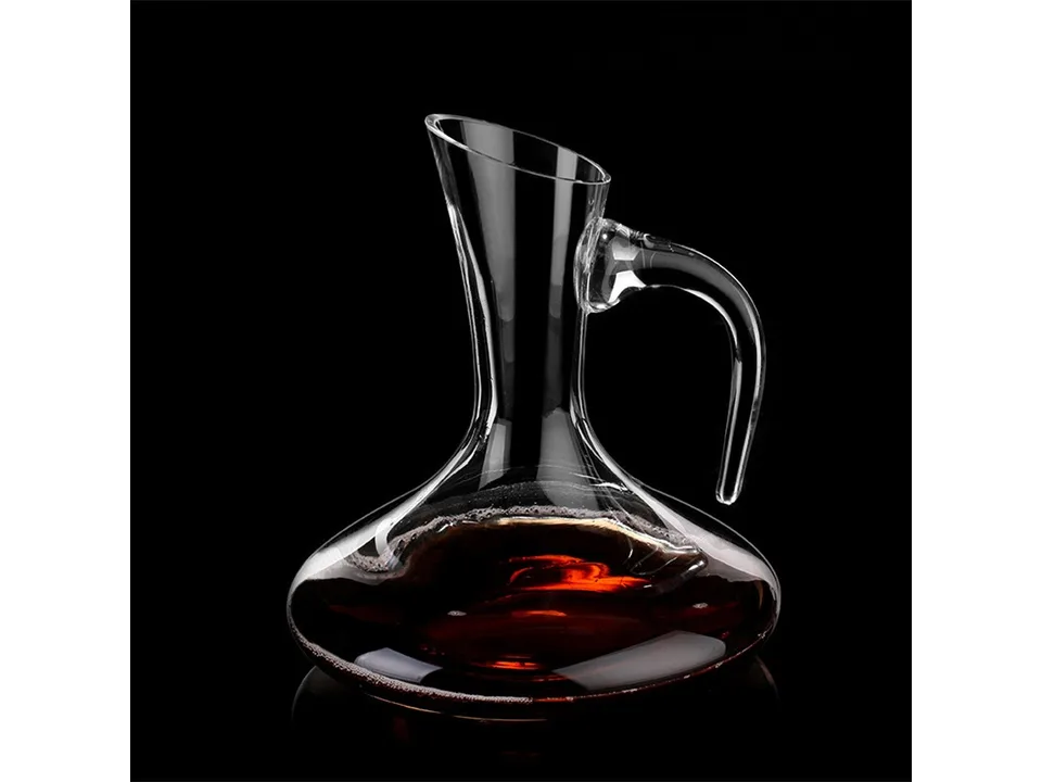 A clear glass wine decanter with a handle, filled with a small amount of red wine, on a black background.