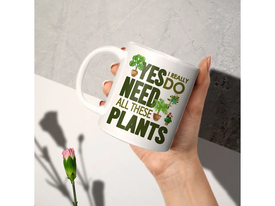 A hand holding the white ceramic mug with a plant-themed design.