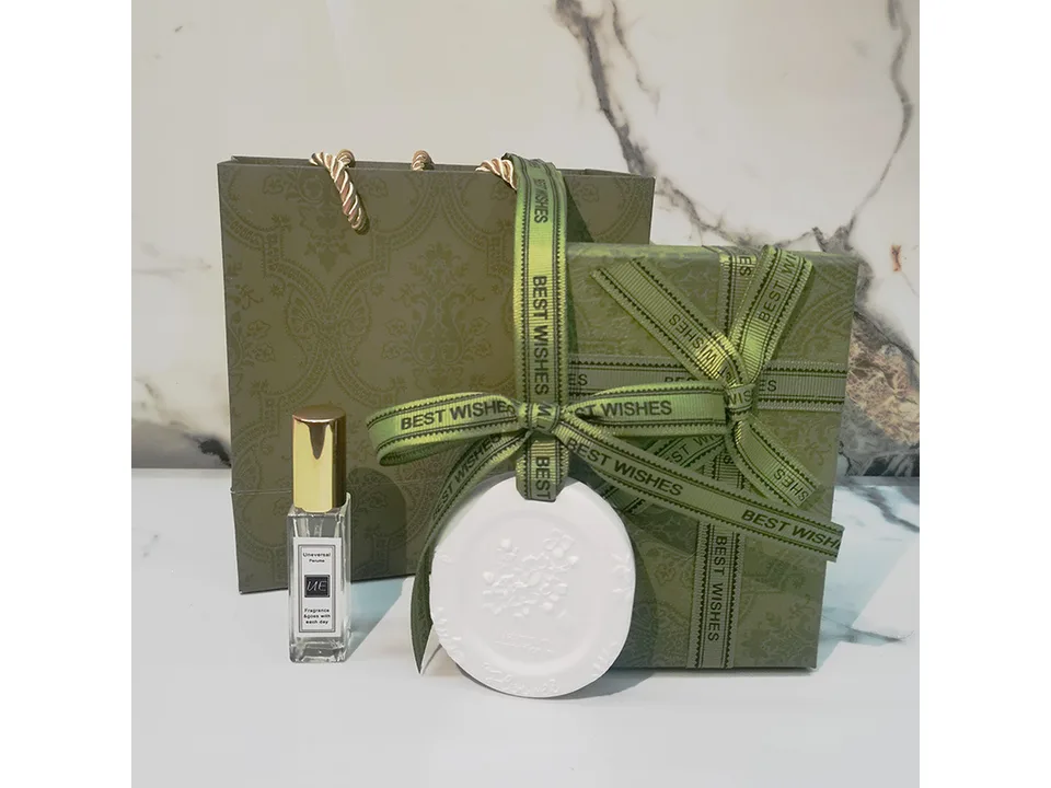 A gift set containing a green gift bag, a ribbon-wrapped gift box, a perfume bottle, and a floral fragrance stone.