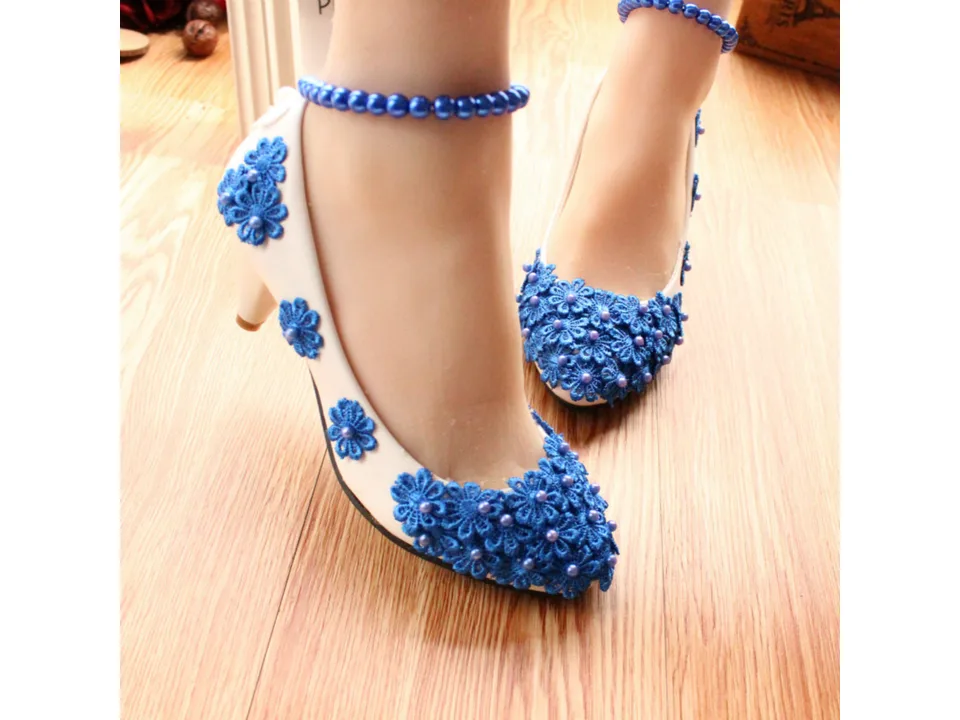 Side view of white high heels with blue floral lace and pearl embellishments worn on feet.