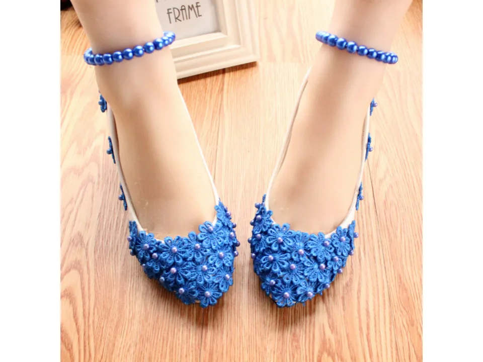 A pair of white high heels with blue floral lace and pearl embellishments worn on feet with matching anklets.