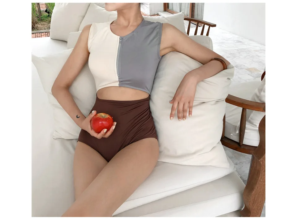 A woman wearing a colorblock cutout one-piece swimsuit while sitting on a couch.