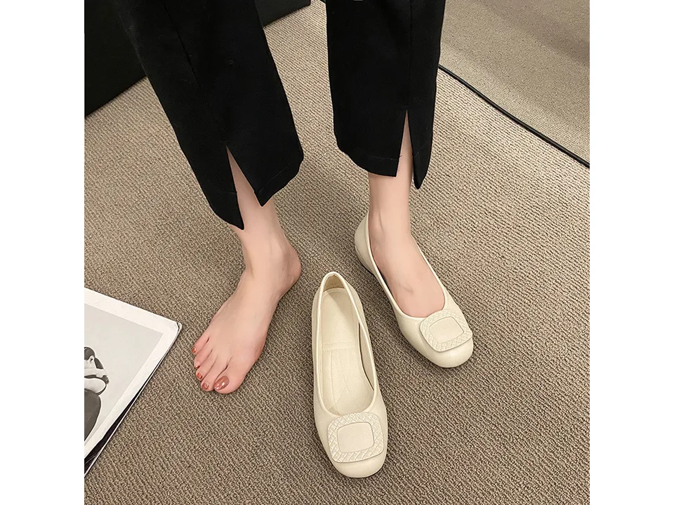 A person wearing beige low heel pumps with a square buckle detail.
