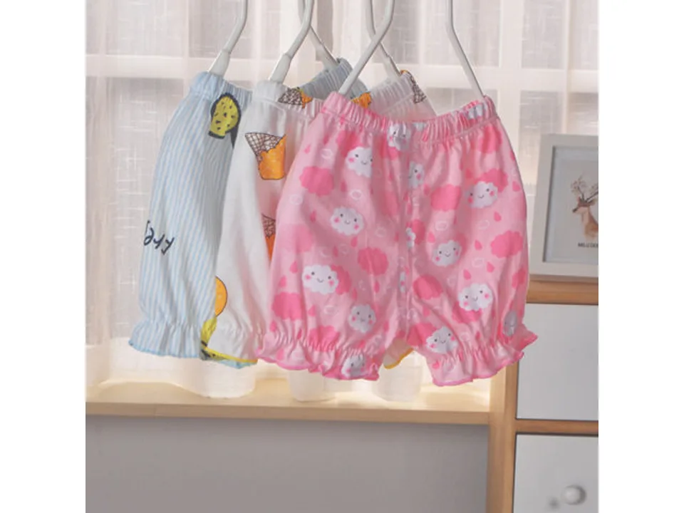 Three pairs of baby bloomer shorts hanging on hangers in front of a window.