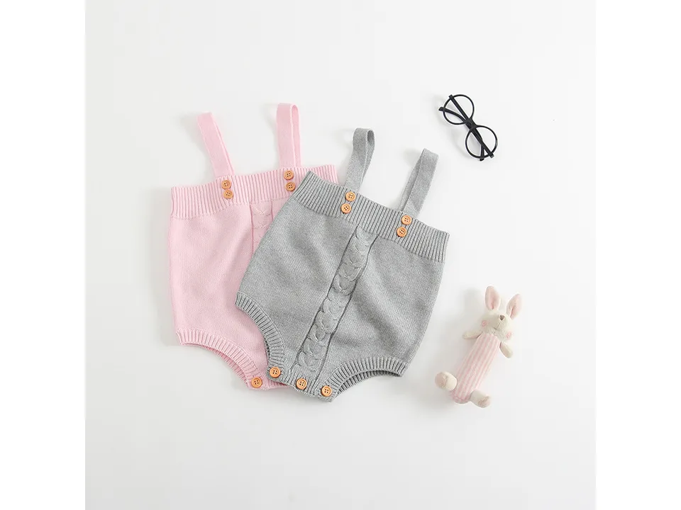 Pink and grey knitted baby rompers displayed together with a toy and glasses.