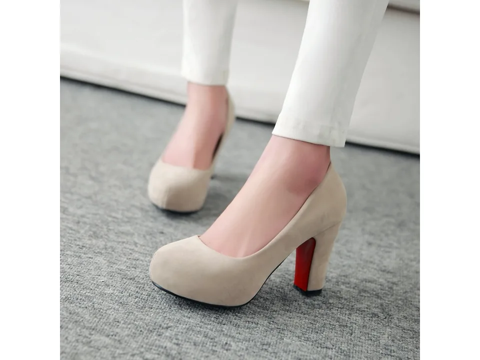 A pair of beige suede chunky heel pumps worn on feet.