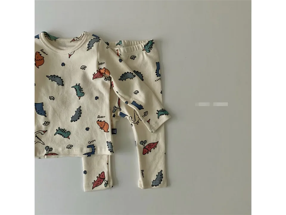 Cream-colored infant pajama set with dinosaur print.