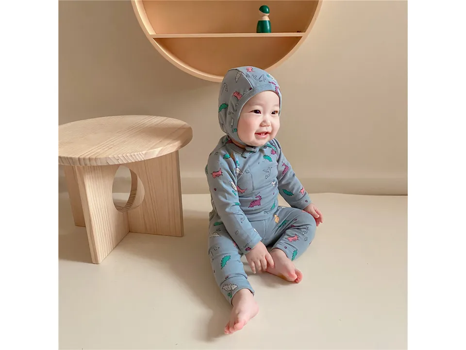 A baby wearing the light blue dinosaur print pajama set and matching hat.