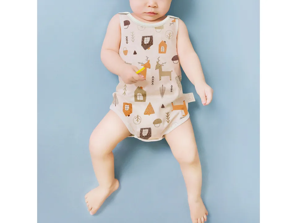 A baby lying down wearing the sleeveless romper with a forest and deer print.
