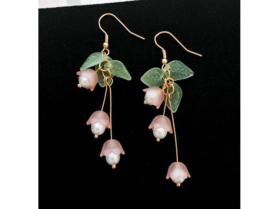 A pair of pink lily of the valley flower dangle earrings with green leaves on a black background.
