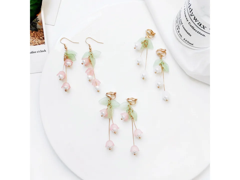 Various lily of the valley earrings arranged on a white plate with a candle in the background.