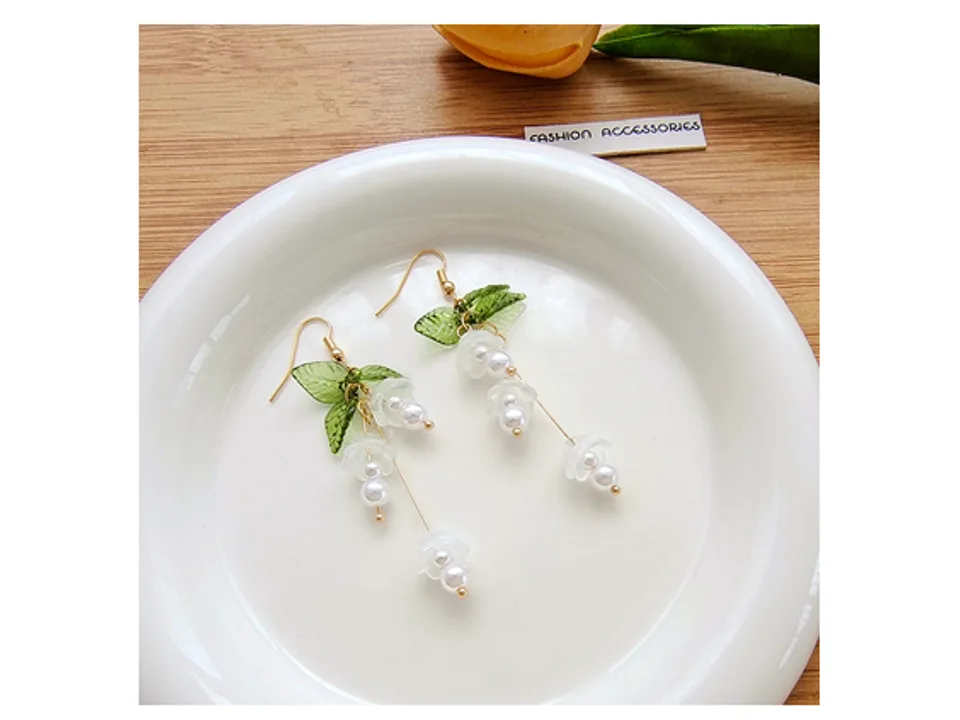A pair of white lily of the valley flower dangle earrings resting on a white plate.