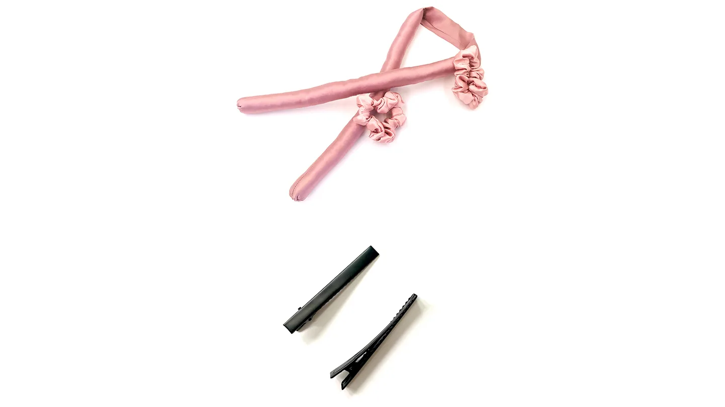 A pink heatless hair curling rod with scrunchies and two black hair clips.
