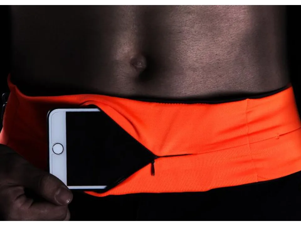 Close-up of a person inserting a smartphone into the zippered pocket of an orange running belt.