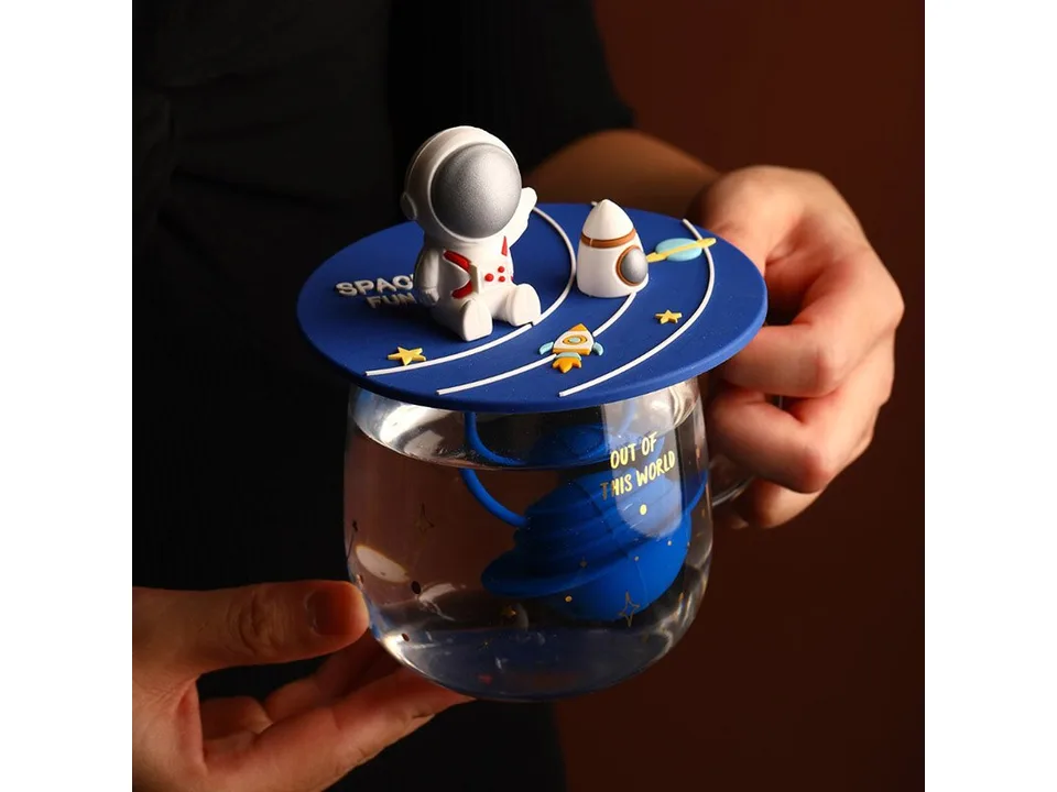 A close-up of a glass mug with an astronaut lid and a planet-shaped tea infuser inside.