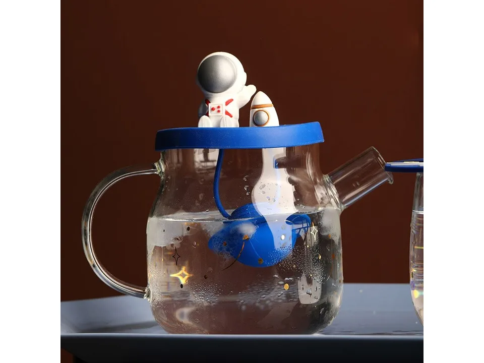 A glass teapot with an astronaut lid and a blue planet-shaped tea infuser submerged inside.