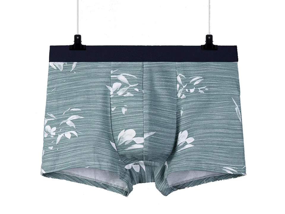 Green boxer briefs with a white leaf pattern hanging on a hanger.