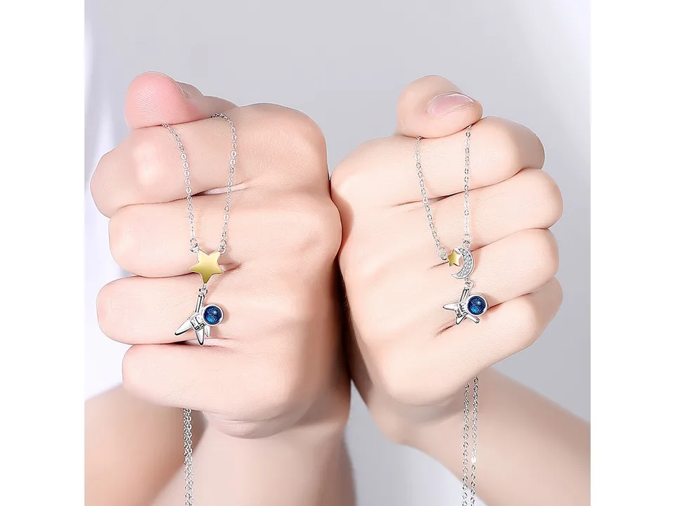 Two hands holding the astronaut couple necklaces.