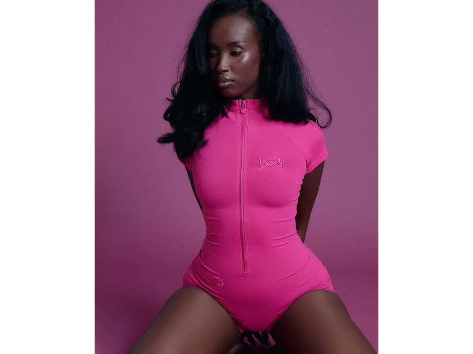 A model wearing a pink short-sleeve zippered yoga jumpsuit.