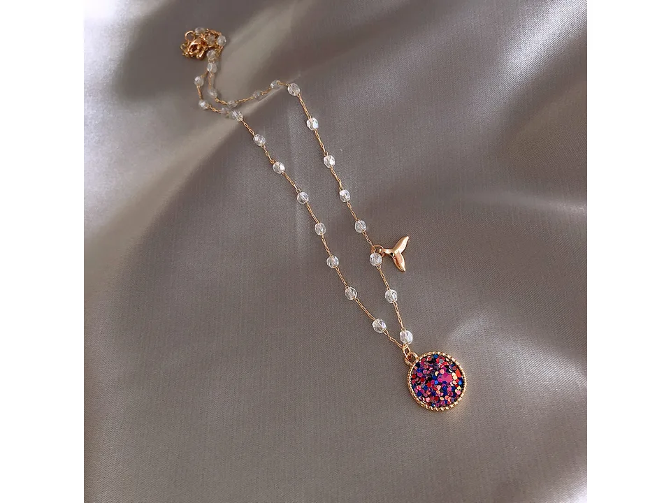 The mermaid necklace laid out on a grey satin background.