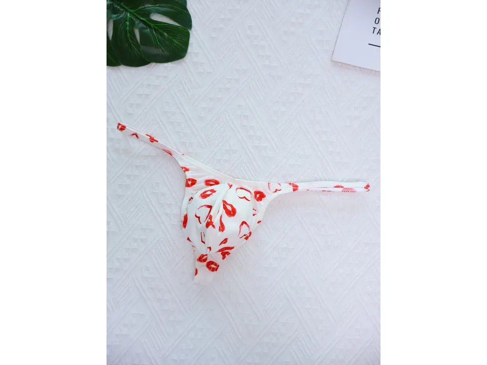 White men's thong with red lip print on a textured background with a leaf.